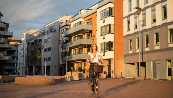 En kvinna cyklar med hus i bakgrunden.